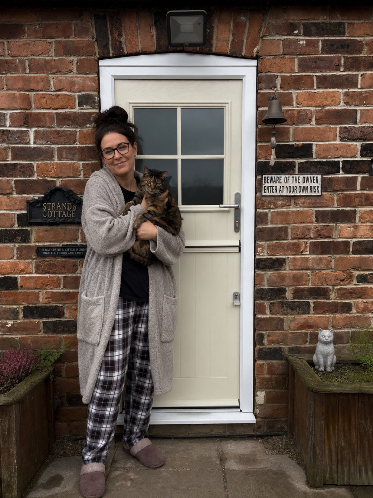 A homeowner holding a cat beside a Merion Stable composite door in Cream